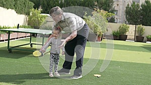 Grandfather teaches little granddaughter to play table tennis