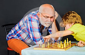 Grandfather teaching grandson to play chess. Childhood and board logic games. Child boy plays chess with grandpa