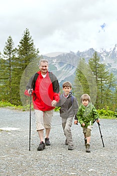 The grandfather and two boys trakking on mountain trail