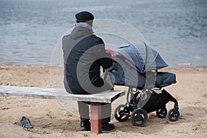 Grandfather walking with a baby stroller on cold and gloomy spring day