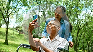 Grandfather in wheelchair and granddaughter using smart phone for selfie in the park. Family life on vacation.