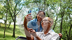 Grandfather in wheelchair and granddaughter using smart phone for selfie in the park. Family life on vacation.
