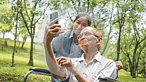 Grandfather in wheelchair and granddaughter using smart phone for selfie in the park. Family life on vacation.