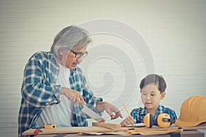 Grandfather worker saw on wood workshop with his grandson for home improvement project