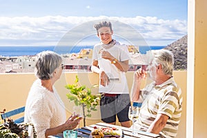 Grandfathers adult mature and teenager nephew enjoy outdoor in the terrace some leisure with food and drinks. ocean and city view photo