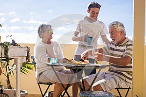 Grandfathers adult mature and teenager nephew enjoy outdoor in the terrace some leisure with food and drinks. ocean and city view photo