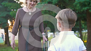 Grandma comes up to her grandson and gives him a book, sunset in the park