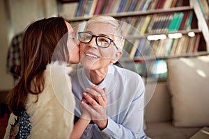 Grandma enjoys a kiss and the love from her granddaughter while spending time at home together. Family, leisure, together