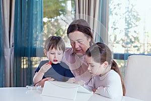Grandma entertaining her little grandchildren with a tablet computer game