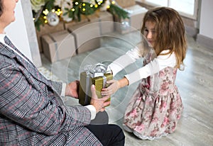 Grandma gives her granddaughter a gift for Christmas. The girl stretches out her hands to the box with the bow. New year, family h