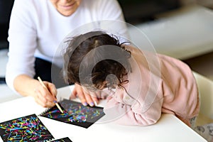 Grandma and granddaughter drawing together with stick on Magic scratch painting paper at home or in class.