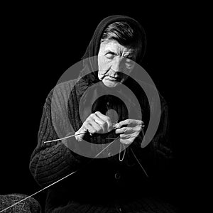 Grandma knitting. Black-and-white low key photograph on black background.