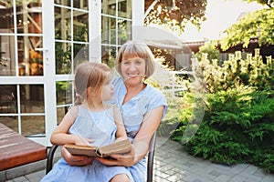 Grandma reads fairy tales to lovely girl while spending time together on sunny terrace near house