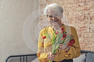 Grandma's Day Mother's Day elderly caucasian woman in a yellow shirt grinning and holding red tulips medium shot