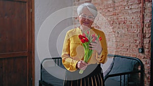 Grandma's Day Mother's Day elderly caucasian woman in a yellow shirt grinning and holding red tulips medium shot
