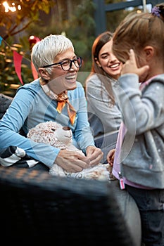 Grandma showing birthday present to her granddaughter. Mother of a little girl in the background. Love, affection, joy, three