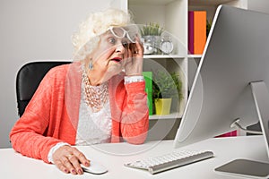 Grandma working at the office and looking at the computer in disbelief photo