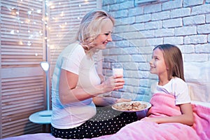 Grandmother brings granddaughter cookies and milk at night at home.