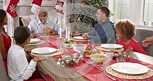 Grandmother brings out Christmas turkey to family seated around table for lunch- everybody applauds as Grandfather prepares to car