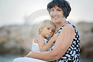 Grandmother and child, cute blond boy and young granny, hugging on the beach