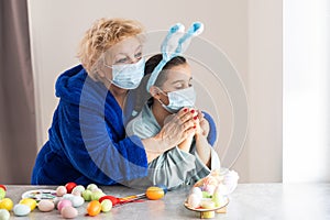 grandmother and children are painting eggs. Happy family are preparing for Easter. Cute little girls wearing bunny ears.