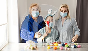 grandmother and children are painting eggs. Happy family are preparing for Easter. Cute little girls wearing bunny ears.