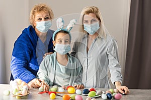 grandmother and children are painting eggs. Happy family are preparing for Easter. Cute little girls wearing bunny ears.