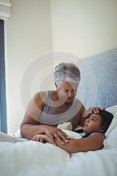 Grandmother comforting sick granddaughter in bed room