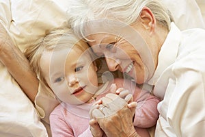 Grandmother Cuddling Granddaughter In Bed