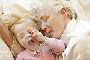 Grandmother Cuddling Granddaughter In Bed