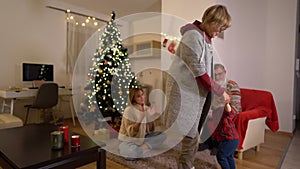 Grandmother is dancing with her grandson near the Christmas tree. Happy family celebrating christmas near the fireplace