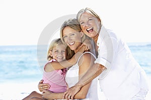 Grandmother With Daughter And Granddaughter Embracing On Beach Holiday