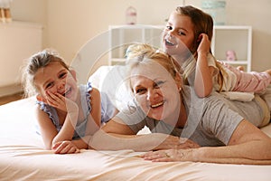 Grandmother enjoying in bed with her little granddaughters. Gran