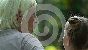 Grandmother giving advices to cute granddaughter, relaxing on bench in park