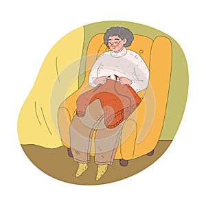 Grandmother in glasses sitting in armchair at home and knitting warm sweater