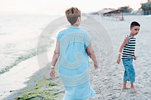 Grandmother with grandchild are resting on sea, running on beach having fun at summer holiday