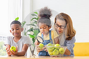 Grandmother and grandchildren playing cheerfully in living room, Kids and mature woman with apple and magnifying glass