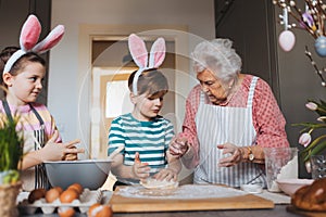 Grandmother with grandchildren preparing traditional easter meals, kneading dough for easter cross buns. Passing down