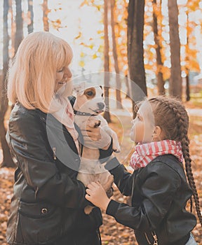 Grandmother with granddaughter in autumn park, girl hugging grandmother and her jack russell terrier dog. Generations