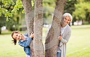 Grandmother and granddaughter behind tree at park