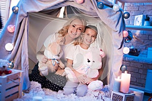 Grandmother and granddaughter with fluffy rabbits in blanket house at night at home.