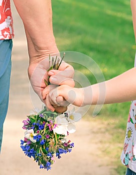 Grandmother and granddaughter hands holding bouquet of wildflowers, close up, love concept