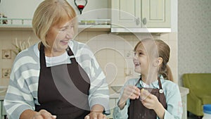 Grandmother and granddaughter having fun in kitchen cooking laughing making biscuits