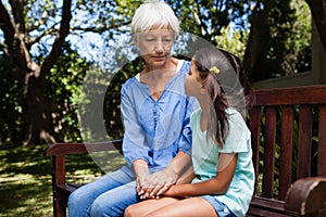 Grandmother and granddaughter holding hands while sitting on bench