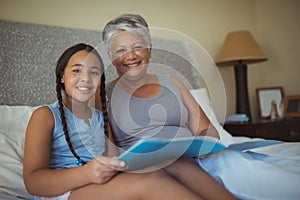 Grandmother and granddaughter holding photo album in bed room