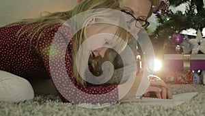 Grandmother and granddaughter lying on the floor near a Christmas tree.