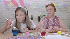 Grandmother and granddaughter painting Easter eggs at home