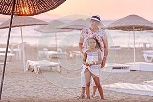 Grandmother and granddaughter posing on the beach at the sunset time. Concept of friendly family