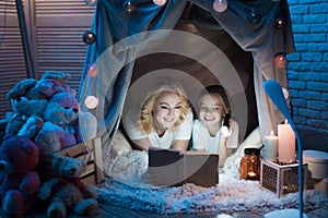 Grandmother and granddaughter are reading book in blanket house at night at home.