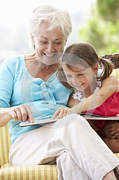 Grandmother And Granddaughter Reading Book On Garden Seat